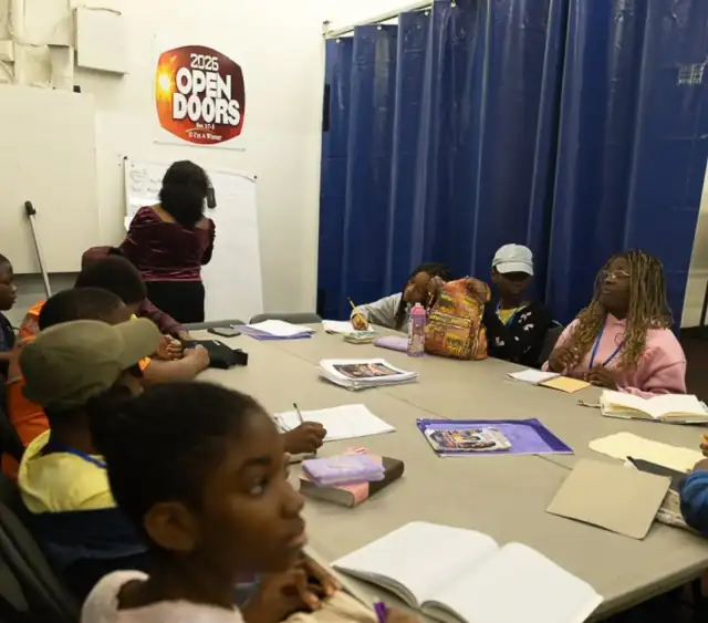 Children and teenagers around a long table with Bibles and notebooks open, the Open Doors 2026 poster on the wall